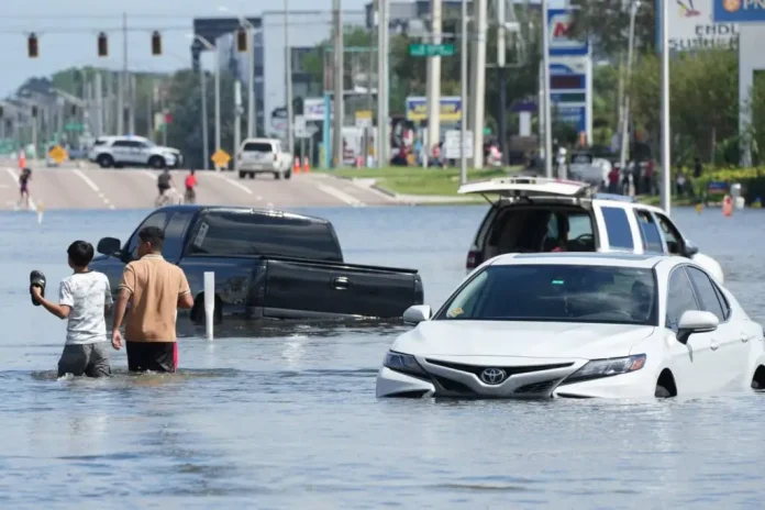 Children walk past vehicles flooded in the water as the streets of the Southeast Seminole Heights section of Tampa due to Hurricane Milton on October 10, 2024 in Florida.